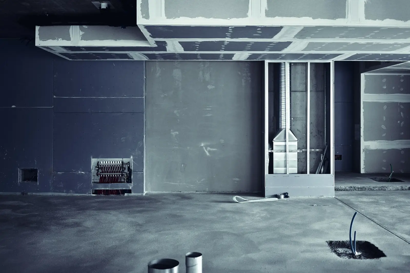 Intérieur en travaux : cloisons en plaques de plâtre, collecteur de plomberie encastré dans le mur, gaine de ventilation, fourreaux qui sortent de la chape.