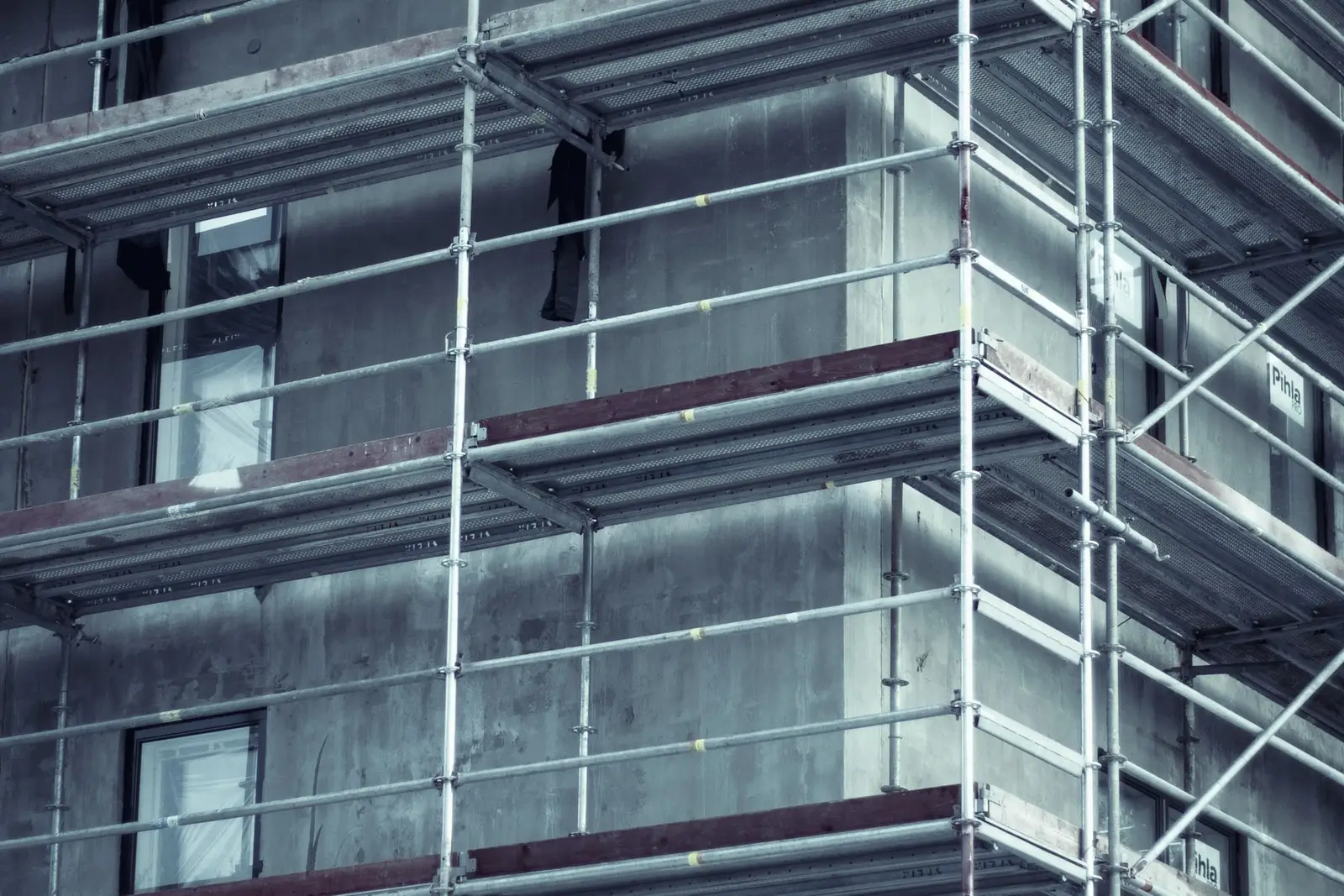 Façade d'un immeuble couverte d'un échafaudage sur toute sa hauteur, avec des garde-corps rouges à chaque niveau.